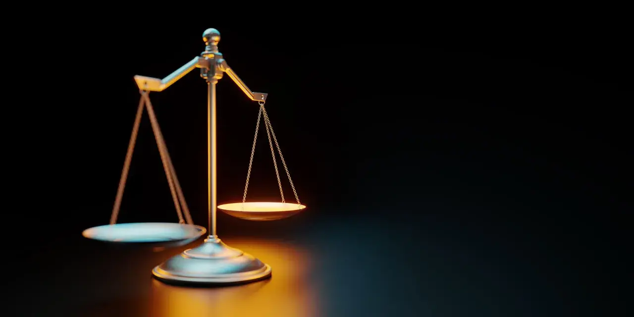Waga szalkowa na ciemnym tle, oświetlona ciepłym światłem.